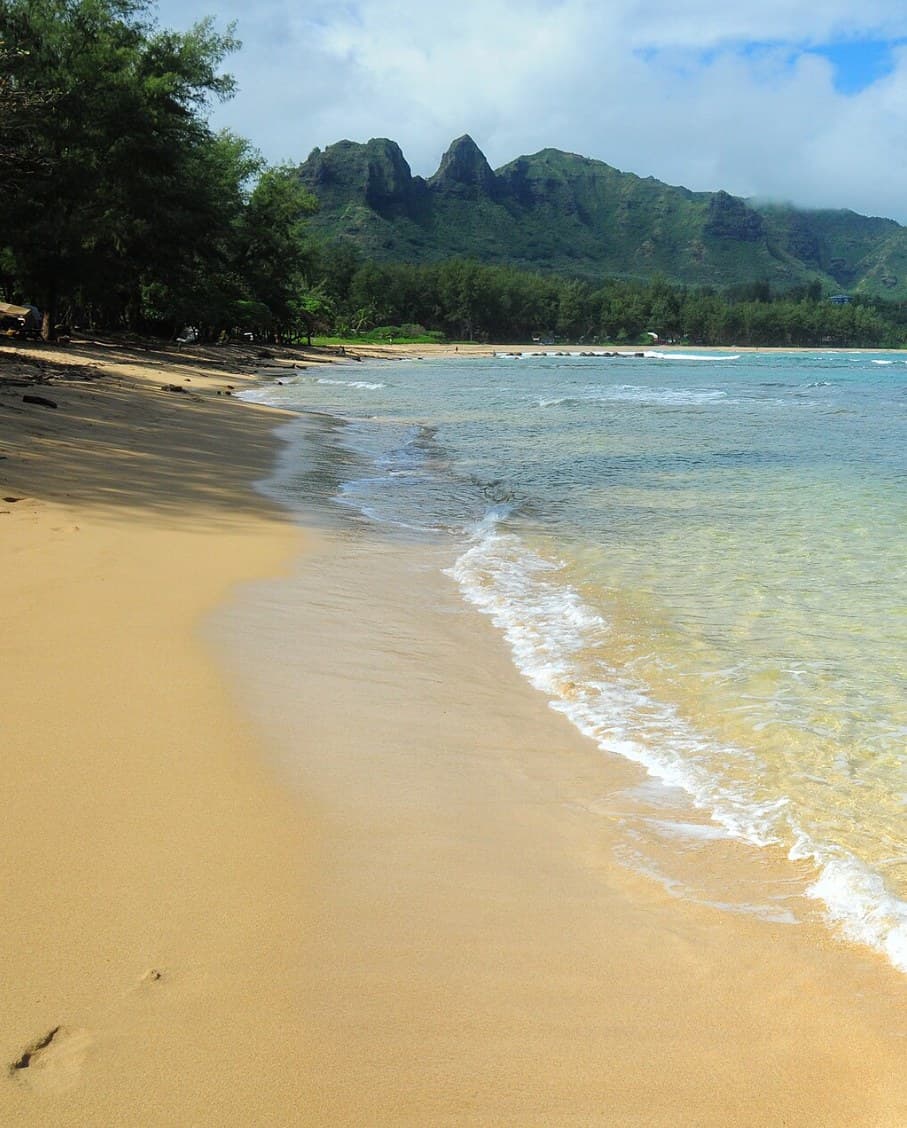 A quiet beach below green mountains — the kind of place Karvan plans for